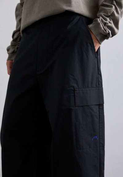 Pantaloni cargo neri con una vestibilità rilassata, dotati di una tasca laterale, una texture liscia e un piccolo logo blu sul lato sinistro anteriore.