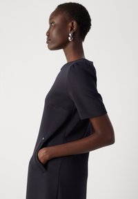 Robe marine à manches courtes, dotée d'une poche et d'un subtil détail de bouton. La texture lisse et la coupe cintrée mettent en valeur le design épuré.