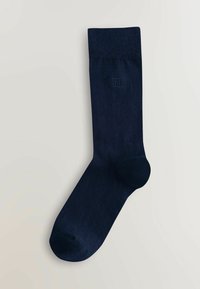 Calzino blu scuro, fino al polpaccio, con un risvolto a coste e un piccolo logo quadrato ricamato vicino alla parte superiore su uno sfondo chiaro.