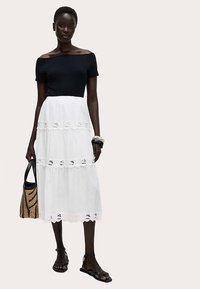 Sort top med bare skuldre kombineret med en hvid flerlagsnederdel med blonderkant. Modellen holder en sort taske og har sorte sandaler på.