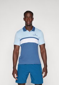 Pikétröja i ljusblått och marinblått med ett vitt vågrätt rand. Har krage och korta ärmar. Logotyp på bröstet, ihop med blå shorts.