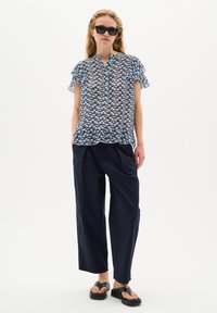 Blusa a maniche corte di colore blu chiaro con motivo astratto blu navy, dotata di chiusura con bottoni e dettagli a volant; abbinata a pantaloni larghi blu navy.