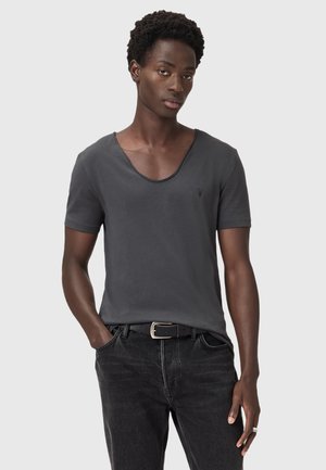 T-shirt noir à manches courtes avec un col en scoop et un logo subtil sur la poitrine, associé à un jean en denim noir et une ceinture noire.
