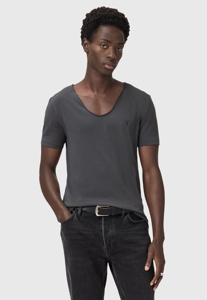 T-shirt corto grigio scuro a maniche corte con scollatura a barca e logo sottile sul petto, abbinato a jeans in denim neri e una cintura nera.