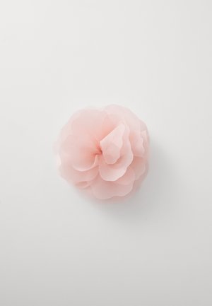 Hellrosa Stoffblume mit geschichteten, transparenten Blütenblättern und einem gerafften Kern, vor einem weißen Hintergrund.