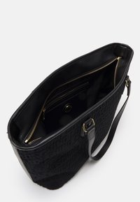 Černá texturovaná kabelka s dvěma uchy, otevřená nahoře, ukazující vnitřní kapsu na zip a hladké podšívkování uvnitř.