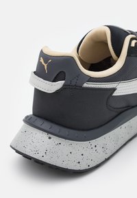 Baskets noires avec une tige texturée, une doublure crème et une semelle grise tachetée. Dotées d'un logo doré et d'un col rembourré pour plus de confort.