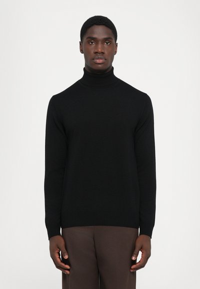 Maglione a collo alto nero con lavorazione a maglia texturizzata, design aderente e polsini a coste. Abbinato a pantaloni marroni per creare contrasto.