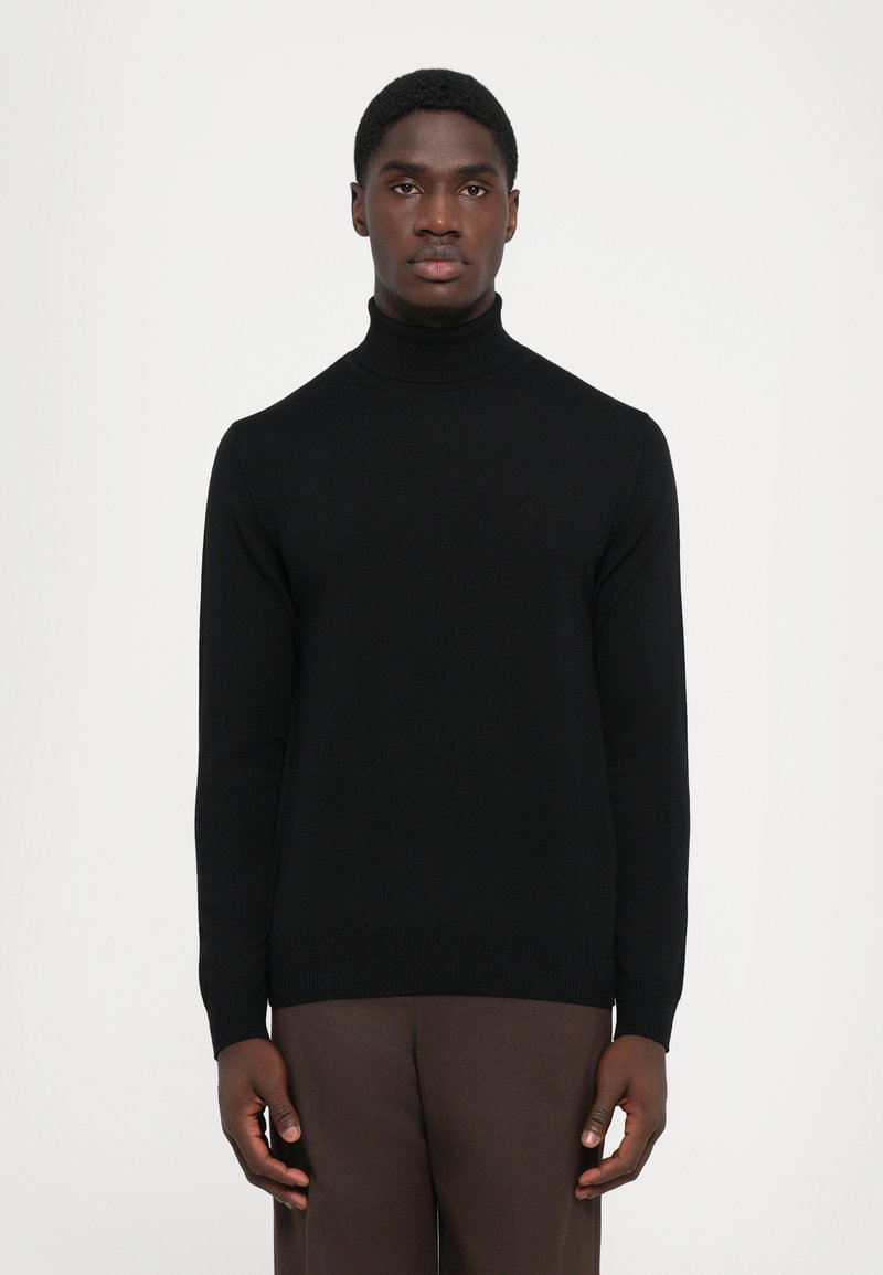 Pulover negru cu guler înalt, cu un tricotaj texturat, design ajustat și manșete côtée. Asortat cu pantaloni maro pentru contrast.