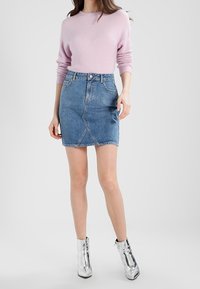 Ljusrosa tröja med lång ärm, kombinerad med en blå denim minikjol med diagonala sömmar. Metalliska anklar boots fulländar outfiten.