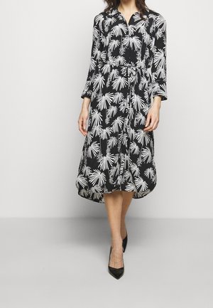 Un vestido negro con un patrón de hojas de palma blancas, mangas largas, cuello con botones, cintura ajustada y falda fluida, combinado con tacones negros.