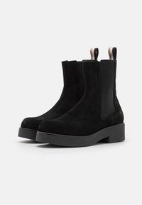 Černé suede kotníkové boty s elastickými bočními panely, texturovanou černou platformou a poutky s hnědými a bílými pruhy.