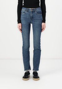Blue denim jeans with a straight-leg fit, five pockets, a button closure, and subtle faded detailing. Paired with black sneakers.