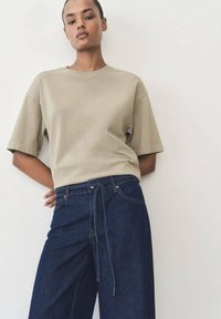Beige katoenen T-shirt met korte mouwen, gecombineerd met donkerblauwe wijde jeans met een trekkoord en voorzakken.