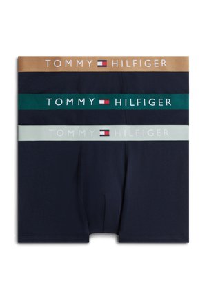 Pile de trois boxers bleu marine avec des ceintures en beige, vert foncé et gris clair, chacun montrant le logo et le drapeau Tommy Hilfiger.