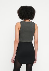 Sötét olíva színű, bordázott anyagból készült, kivágott, ujjatlan top, kerek nyakkivágással és nyers szegéllyel. Magas derekú fekete szoknyával párosítva.