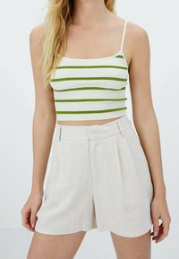 Femme portant un crop top blanc côtelé avec des rayures horizontales vertes et un short beige taille haute sur un fond uni.