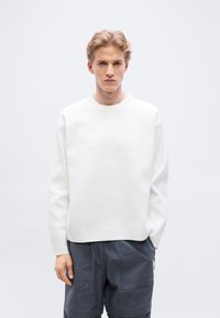 Λευκό φούτερ με υφασμένο λογότυπο, με στρογγυλή λαιμόκοψη και χαλαρούς ώμους, συνδυασμένο με σκούρες μπλε cargo βερμούδες.