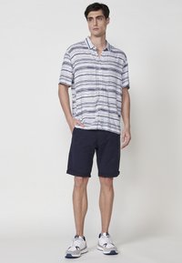 Košela s krátkym rukávom, s golierom, modro-biele horizontálne pruhy, v kombinácii s námorníckymi rolovanými šortkami a bielymi športovými topánkami s modrými akcentmi.