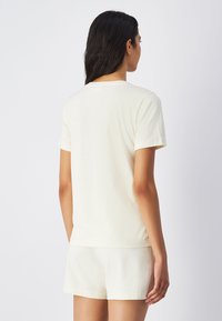 T-shirt a maniche corte color crema realizzata in tessuto morbido, con colletto girocollo classico e una vestibilità rilassata, abbinata a pantaloni corti coordinati.