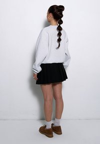 Szary, oversize'owy sweter, czarna spódnica z plisami, brązowe buty, białe skarpetki, włosy związane w wysoki kucyk z falującym detalem, widok z tyłu.