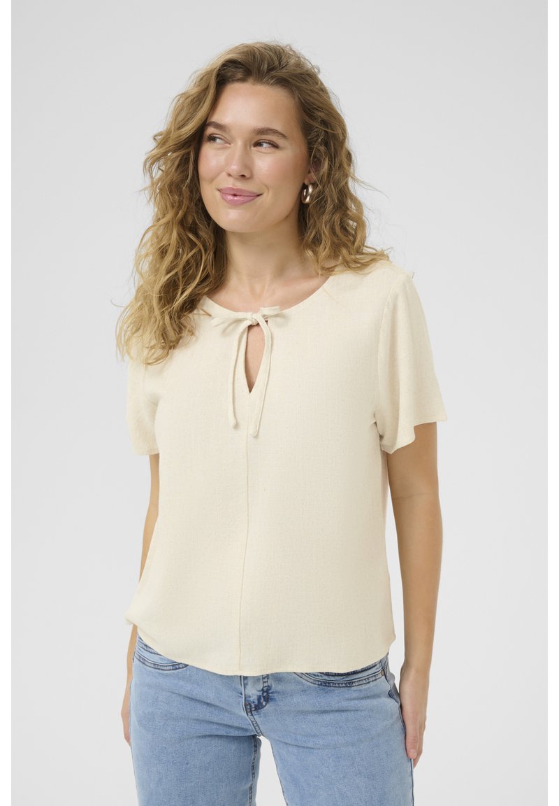 Blusa a maniche corte color crema con scollo rotondo e dettaglio con fiocco nella parte anteriore. Realizzata in tessuto leggero e texturizzato.