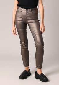 Metalen bronzen jeans met een aansluitend ontwerp, hoge taille, subtiele glans en vijf zakken, gecombineerd met zwarte instappers.