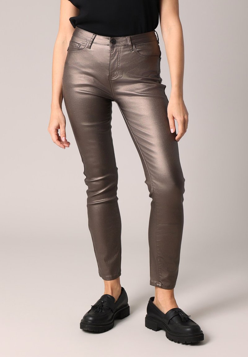 Metalen bronzen jeans met een aansluitend ontwerp, hoge taille, subtiele glans en vijf zakken, gecombineerd met zwarte instappers.