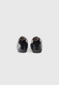 Baskets noires avec une tige en cuir lisse et en daim, contrefort semi-rigide et semelle extérieure en caoutchouc texturé. Comprend un marquage subtil sur le talon.
