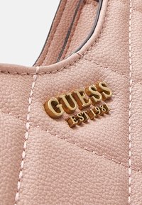 Borsa in materiale sintetico rosa trapuntato con logo dorato "GUESS" e dettaglio "EST 1981", caratterizzata da cuciture evidenti e una texture liscia.
