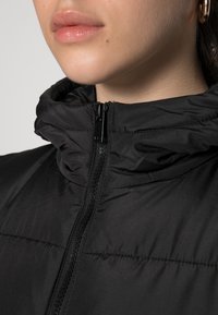 Närbild av en persons nedre ansikte och nacke, iförd en svart zip-up puffjacka med dragkedjan helt stängd.