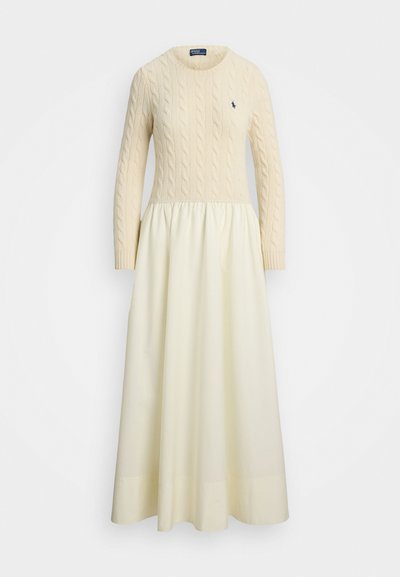 Vestido de malha trançada em creme com mangas longas, gola redonda e saia fluida franzida, apresentando um pequeno logótipo escuro no peito.