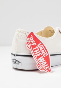 Leichte beige Leinensneaker mit weißer Sohle und schwarzem Streifen. Mit rotem und weißem Etikett mit der Aufschrift "VANS OFF THE WALL." Strukturiertes Gummilaufsohle.