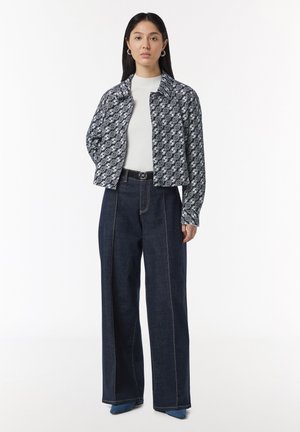 Przycięta granatowa kurtka w wzór, noszona na białym golfie, w połączeniu z wysokim stanem ciemnoniebieskimi spodniami typu wide-leg z kontrastowym szwami.