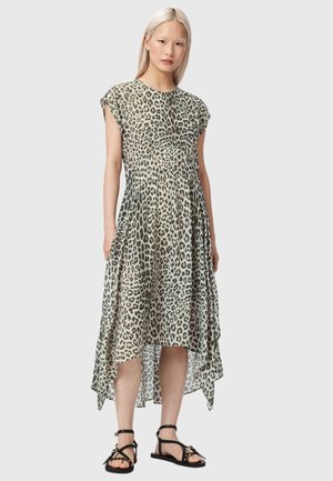 Femme portant une robe sans manches avec un ourlet asymétrique à imprimé léopard gris et noir et des sandales plates noires, debout devant un fond uni.