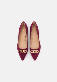 Escarpins en suede bordeaux à talons hauts avec un bout pointu et un accent en chaîne dorée sur le dessus. Doublure intérieure lisse et semelle rembourrée.