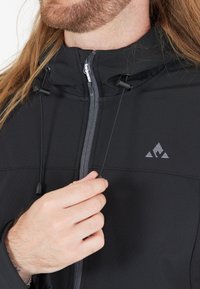 Schwarze Jacke mit Reißverschluss und hohem Kragen. Mit verstellbaren Zugbändern und einem Logo auf der Brust. Glattes, strukturiertes Material.