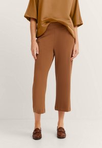 Braune, kurz geschnittene Hose aus glattem Stoff, mit einem elastischen Bund und einer lockeren Passform. Kombiniert mit einem passenden, übergroßen Oberteil.