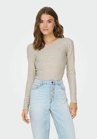 Top a maniche lunghe a coste color grigio chiaro, con scollatura rotonda e polsini scallopati, abbinato a jeans leggeri a vita alta color blu chiaro con chiusura a bottoni.