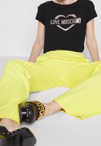 Svart kortärmad t-shirt med metallisk "LOVE MOSCHINO" logotyp; ljusgul vid byxa; svarta skor med gulddetaljer och nitar.