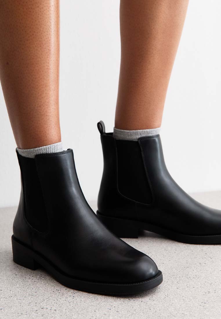 Botas de tobillo de cuero negro con acabado suave, que cuentan con paneles laterales elásticos, un tacón bajo y una tira de agarre en la parte posterior.