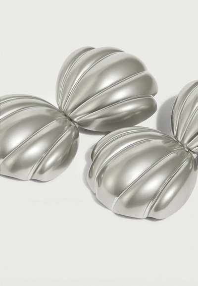 Δύο λαμπερά ασημί μεταλλικά αντικείμενα σε σχήμα κογχής, συνδεδεμένα στο κέντρο σε λευκό φόντο.