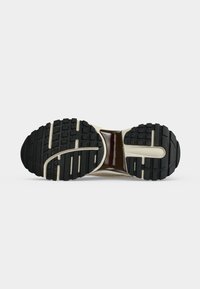 Semelle de chaussure avec des crans en caoutchouc noir et des accents beige, présentant un design texturé et segmenté pour la traction et la stabilité.