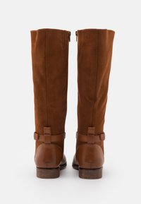 Bottes hauteur genou en daim marron avec fermeture éclair, accents en cuir et talon en bois. Comprennent une bride décorative autour de la cheville.