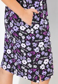 Kukkamekko mustalla taustalla, jossa on violetteja ja valkoisia kukkia. Pehmeä kangas, sivutasku, polvimittainen ja siinä on pieni halkio.