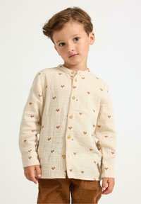 Hellbeige Hemd mit braunen Fuchs-Muster, weicher Textur und runder Kragen, kombiniert mit braunen Cord-Hosen.
