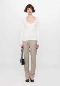 White long-sleeve scoop neck top paired with beige tailored pants and black flats. A small black handbag is held in the left hand.
