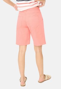 Koraalroze shorts met een ontspannen pasvorm, voorzien van achterzakken en een platte tailleband. Gemaakt van lichte stof. Eenvoudige zoom. Sandalen zichtbaar.