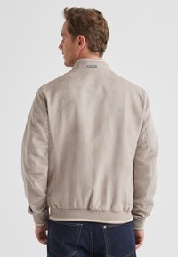 Beige Bomberjacke mit glatter, wildlederähnlicher Textur, gerippten Bündchen und Saum sowie abgerundetem Kragen. Verfügt über minimale Nähte und dezentes Branding.