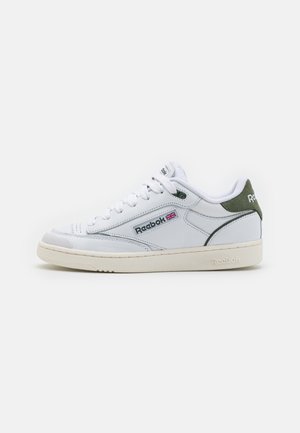 Sneakers bianchi in pelle con finitura testurizzata, dettagli verdi sul tallone e suola in gomma color crema. Presentano lacci tondi e logo.
